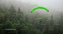 Skydiver Descending with Green Parachute over Misty Forest
