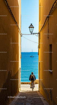 Cyclist in Narrow Alleyway with Serene Sea View