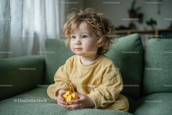 Kręcone dziecko odpoczywające na zielonej sofie w żółtym sweterku