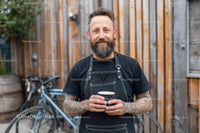 Tattooed Barista Holding Coffee in Rustic Setting