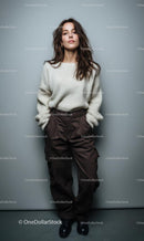 Woman in Cozy Sweater and Brown Pants Against Gray Wall