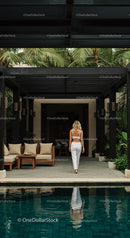 Woman Walking by Luxury Villa Pool Amidst Palm Trees