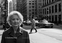 Elderly Woman in Busy City Street Surrounded by Vintage Cars