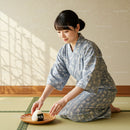 Young woman in kimono placing rice ball on wooden plate