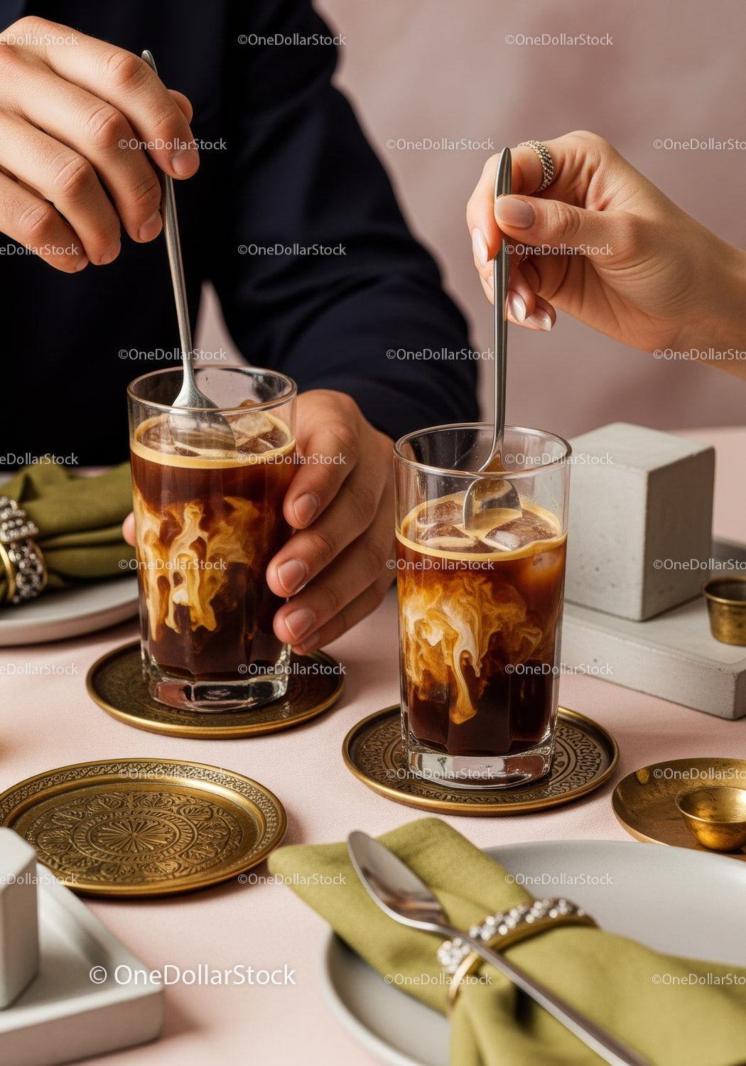 Two People Stirring Iced Coffee in Stylish Glasses on Elegant Table