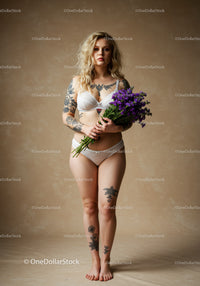 Stylish Woman with Tattoos Holding Purple Flowers in Lingerie