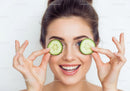 Joyful Woman Holding Cucumber Slices Over Eyes in Bright Studio