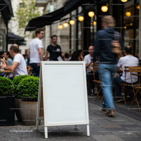Blank street sign by bustling outdoor cafe in city
