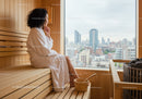 Woman Sitting in Wooden Sauna with City View in Modern Wellness Center