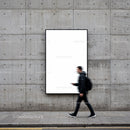 Blurred man walking past blank urban poster on concrete wall
