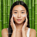 Young Woman Applying Facial Cream on Cheeks with Green Bamboo Background
