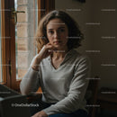 Young Woman Sitting Near Window with Thoughtful Expression in Cozy Interior