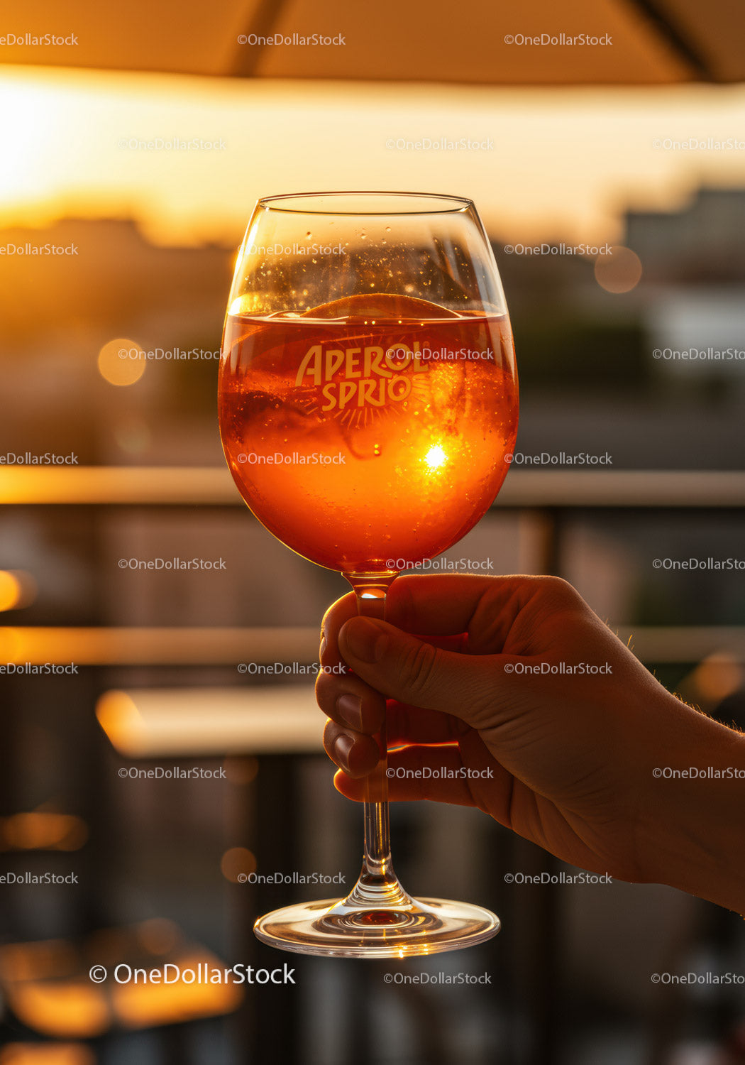 Hand Holding Aperol Spritz Against Sunset Glow