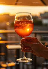 Hand Holding Aperol Spritz Against Sunset Glow