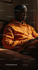 Young Man Wearing Orange Hoodie and Black Beanie Sitting Thoughtfully