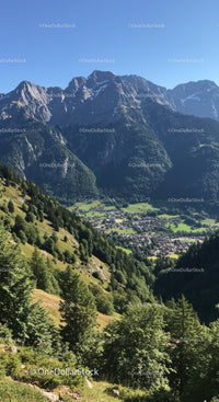 Majestic Mountain Range with Green Forest and Small Village Under Clear Blue Sky