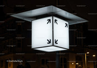 Illuminated cube street sign with black arrows at night
