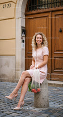 Smiling woman in pink dress sitting on stone post outdoors