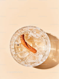 Glass of iced water with cinnamon stick on beige surface