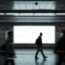 People walking past empty billboard in subway station