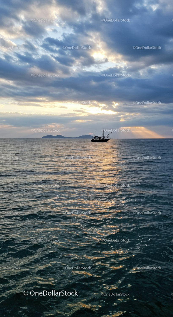 Serene Sunset Over Ocean with Sailing Boat and Cloudy Sky