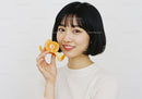 Young Woman Holding Fresh Tangerine Slice with Bright Smile