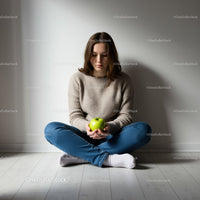 Thoughtful young woman sitting with green apple indoors