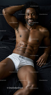 Smiling muscular man relaxing on dark bed in white briefs