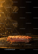 Juicy steak grilling with flames and smoke at night
