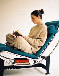 Woman in cozy knitwear reading book on modern chair
