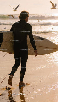 Surfer in wetsuit walking on sandy beach at sunset