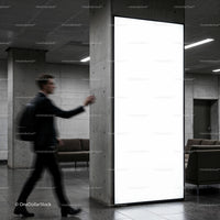 Businessman walking past illuminated blank billboard indoors