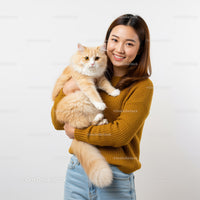 Smiling woman holding fluffy cream cat indoors
