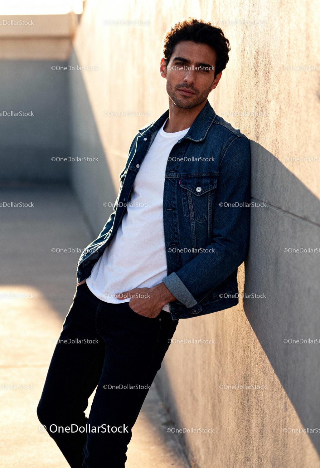 Casual man leaning on sunlit urban concrete wall