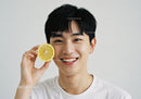 Young Man Smiling While Holding Lemon Slice in Bright Indoor Setting