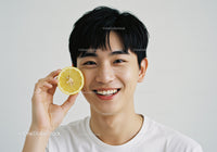 Young Man Smiling While Holding Lemon Slice in Bright Indoor Setting