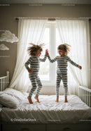Two children in striped pajamas jumping on bed