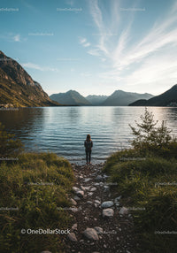 Serene woman standing on rocky lakeside trail with majestic mountains