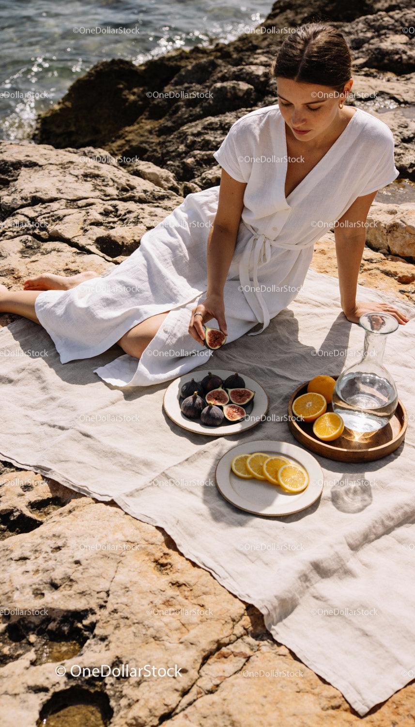 Woman enjoying fresh figs and citrus on rocky shore