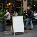 Blank white sandwich board outside busy city cafe