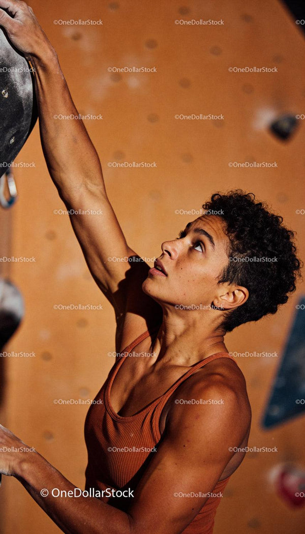 Focused female climber reaching for grip indoors