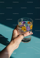 Hand Holding Glass of Water with Floating Pansy Flowers