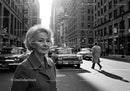 Elderly Woman in Busy City Street Surrounded by Vintage Cars