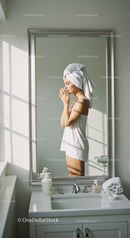 Woman in Towel Reflecting in Bathroom Mirror with Skincare Products