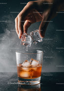 Hand Adding Ice Cubes to Whiskey Glass on Black Surface