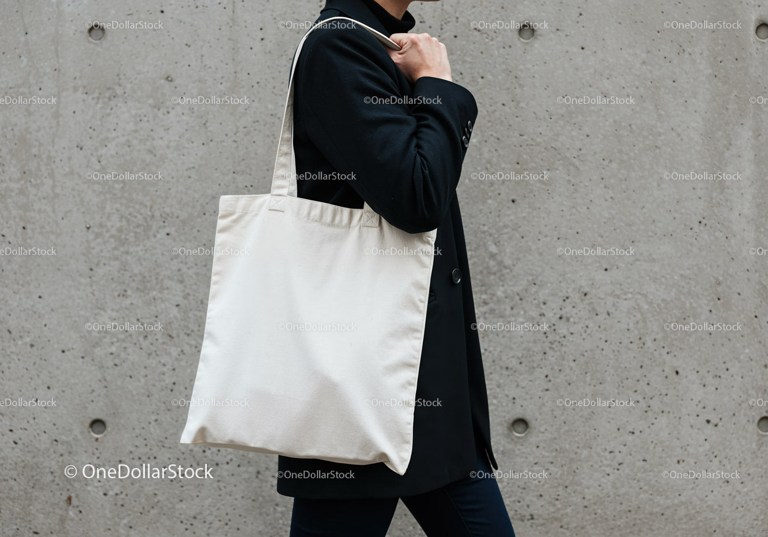 Person carrying plain white tote bag against concrete wall