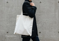 Person carrying plain white tote bag against concrete wall