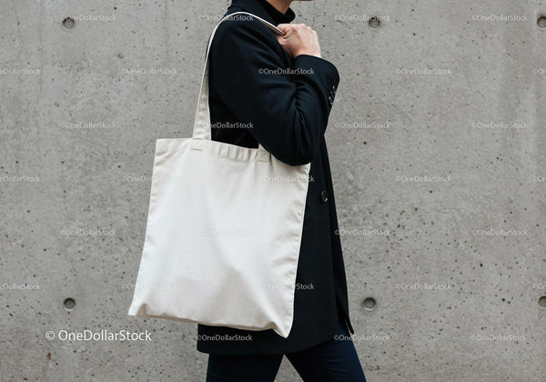 Person carrying plain white tote bag against concrete wall JPG Mockup Image