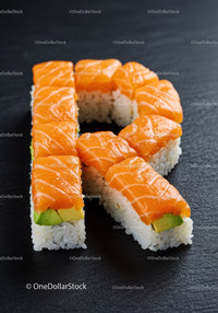 Fresh salmon sushi shaped like the letter R on black slate