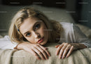 Portrait of a Young Woman with Blonde Hair and Blue Eyes Lying on a Beige Blanket